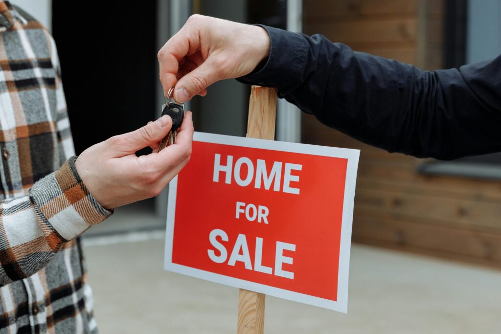 Close-up of a home for sale sign with people exchanging keys.